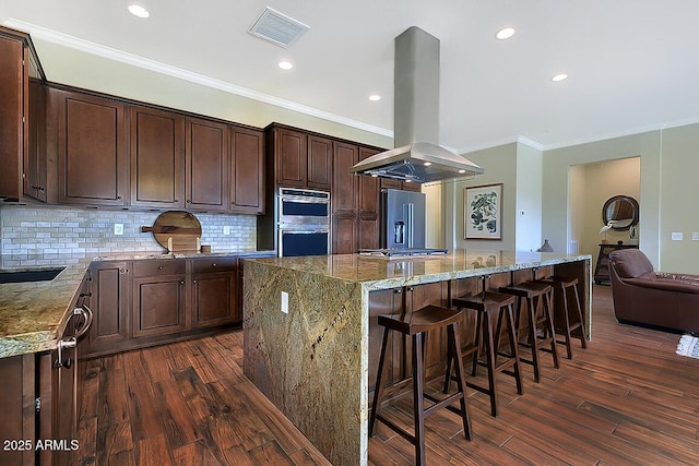 kitchen with dark wood-type flooring, light stone countertops, island range hood, and a spacious island