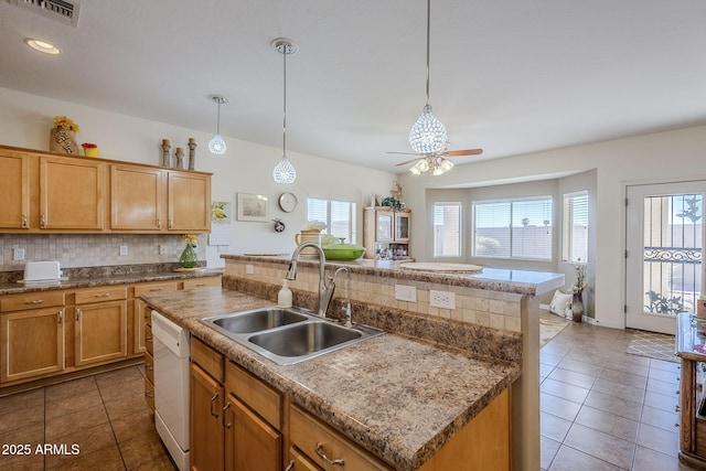 kitchen featuring sink, decorative light fixtures, a center island with sink, dishwasher, and backsplash