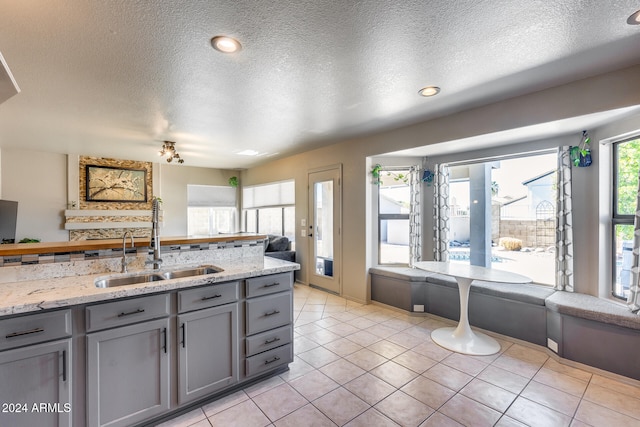 kitchen with gray cabinetry, light stone counters, a textured ceiling, and sink