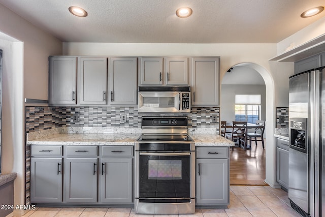 kitchen with stainless steel appliances, light stone countertops, light tile patterned floors, and gray cabinets