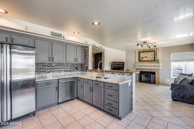 kitchen with kitchen peninsula, light tile patterned flooring, sink, gray cabinets, and stainless steel appliances