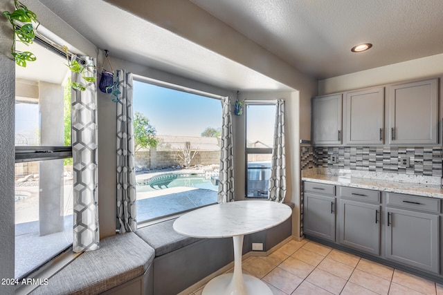 kitchen with gray cabinets, decorative backsplash, light stone counters, and light tile patterned floors