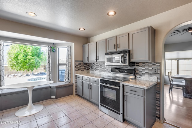 kitchen featuring decorative backsplash, gray cabinetry, stainless steel appliances, a textured ceiling, and ceiling fan