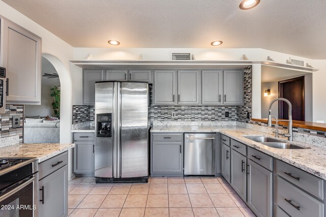 kitchen featuring stainless steel appliances, sink, light tile patterned floors, gray cabinets, and tasteful backsplash