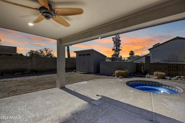 patio terrace at dusk featuring a storage shed, an in ground hot tub, and ceiling fan