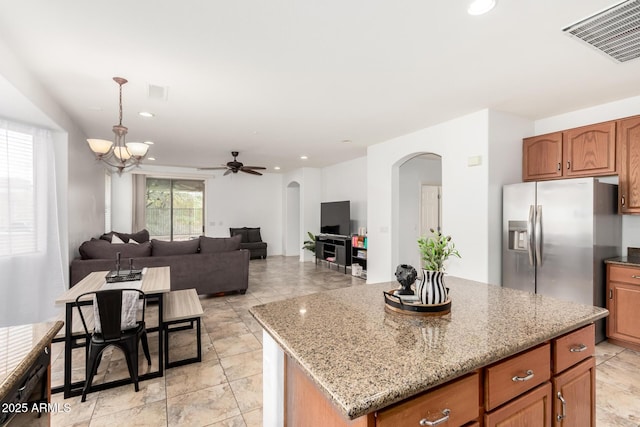 29751 N 119th Ln, Peoria, AZ 85383 - kitchen featuring arched walkways, stainless steel fridge with ice dispenser, light stone countertops, a center island, and brown cabinets