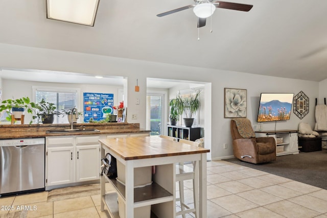 kitchen featuring light tile patterned flooring, wood counters, sink, stainless steel dishwasher, and white cabinets