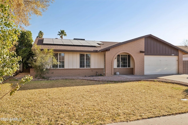 ranch-style home with a garage, a front lawn, and solar panels