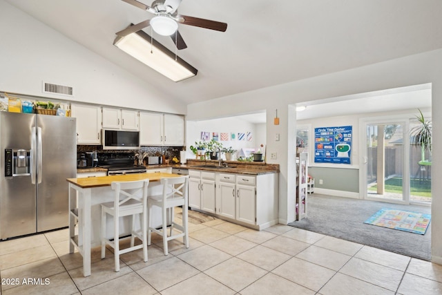 kitchen with lofted ceiling, light tile patterned floors, stainless steel appliances, and white cabinets