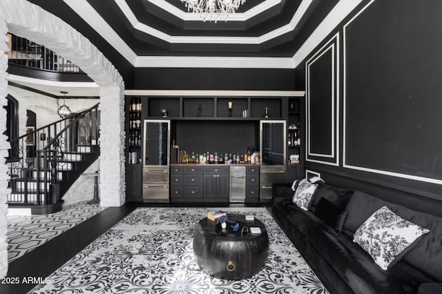 living room featuring decorative columns, a notable chandelier, stairway, bar area, and ornamental molding