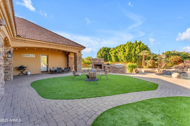 view of yard with exterior kitchen, an outdoor stone fireplace, and a patio