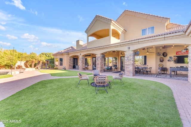 back of property with a chimney, stucco siding, a patio area, and a yard