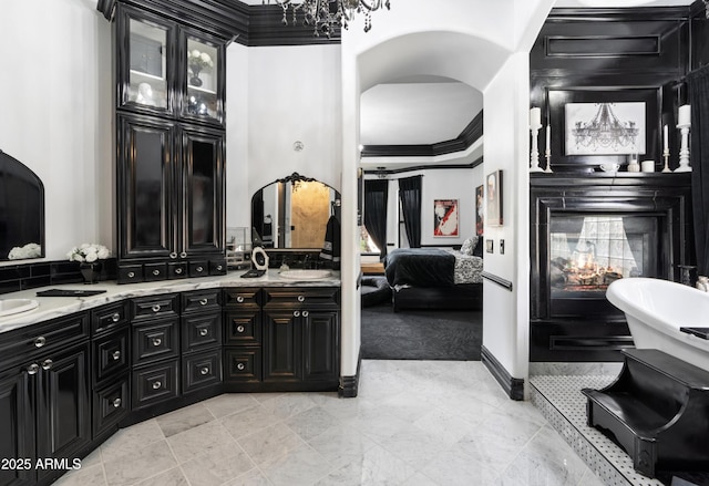 ensuite bathroom with a chandelier, double vanity, ornamental molding, connected bathroom, and a multi sided fireplace