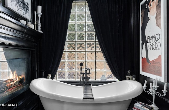 full bathroom featuring a soaking tub, a sink, a healthy amount of sunlight, and a lit fireplace