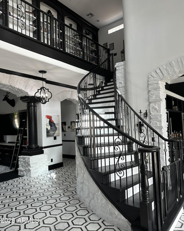 stairway featuring decorative columns, visible vents, arched walkways, baseboards, and a towering ceiling