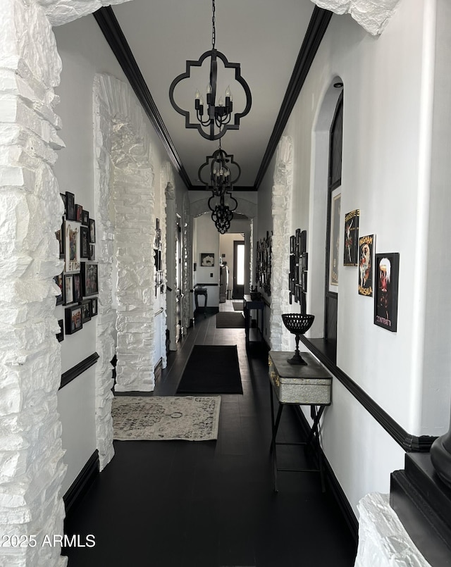 corridor featuring baseboards, arched walkways, ornamental molding, and an inviting chandelier