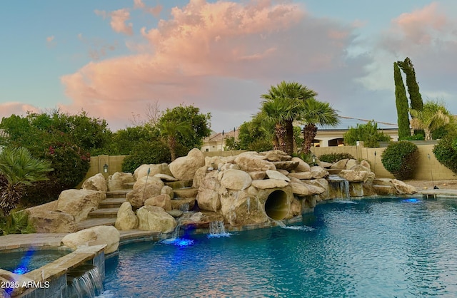 pool at dusk featuring an in ground hot tub, fence, and a fenced in pool