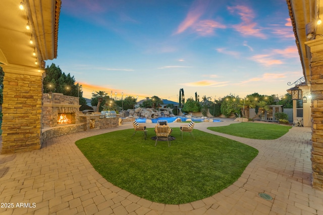 yard at dusk with exterior kitchen, an outdoor stone fireplace, and a patio area