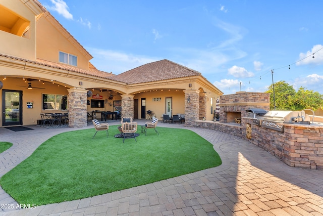 view of patio / terrace featuring area for grilling, exterior kitchen, an outdoor stone fireplace, and ceiling fan