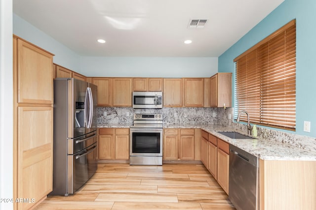 kitchen with backsplash, light wood-type flooring, light stone counters, stainless steel appliances, and sink