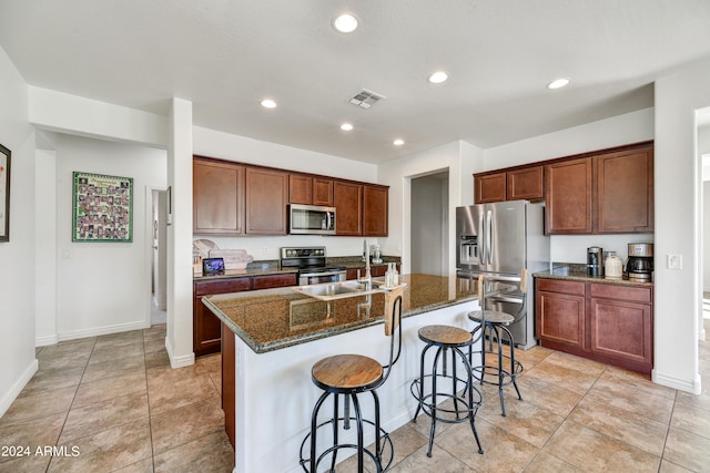 kitchen featuring an island with sink, appliances with stainless steel finishes, a kitchen bar, dark stone counters, and sink