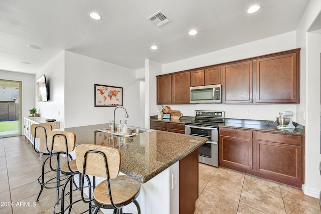 kitchen with a center island with sink, dark stone counters, light tile patterned flooring, sink, and stainless steel appliances