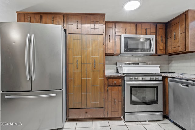 kitchen with decorative backsplash, light tile patterned flooring, light stone counters, and appliances with stainless steel finishes