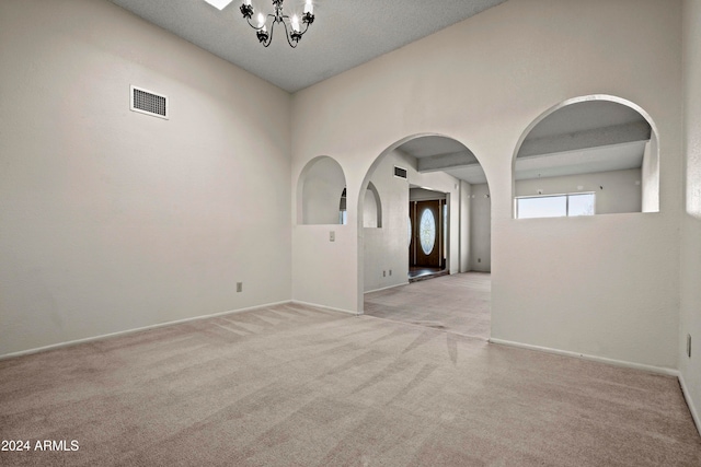 carpeted empty room with a textured ceiling and a notable chandelier