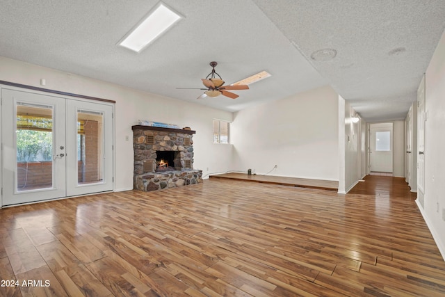 unfurnished living room with hardwood / wood-style floors, ceiling fan, a stone fireplace, and a textured ceiling