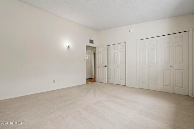 unfurnished bedroom with light carpet, a textured ceiling, and multiple closets