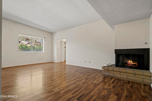 unfurnished living room featuring a textured ceiling, a brick fireplace, and dark wood-type flooring