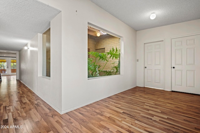 corridor with french doors, hardwood / wood-style floors, and a textured ceiling