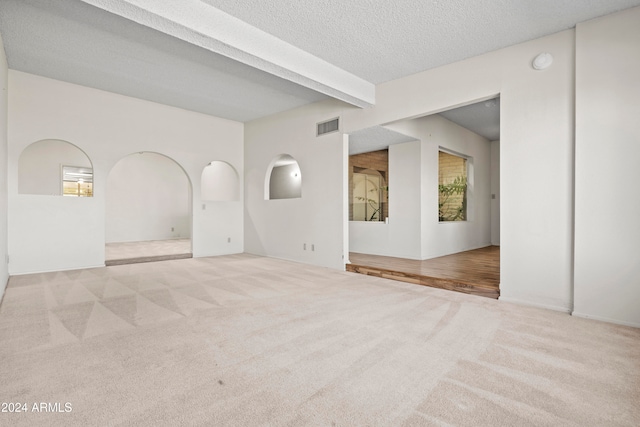 empty room featuring beamed ceiling, a textured ceiling, light colored carpet, and plenty of natural light