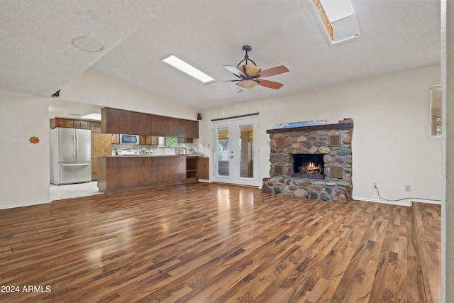 unfurnished living room with french doors, vaulted ceiling, light hardwood / wood-style flooring, ceiling fan, and a fireplace