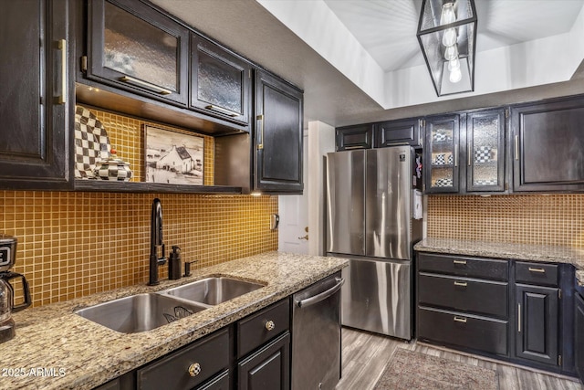 kitchen featuring sink, tasteful backsplash, appliances with stainless steel finishes, light stone countertops, and light hardwood / wood-style floors