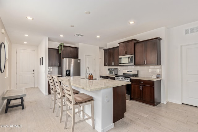 kitchen featuring sink, an island with sink, light hardwood / wood-style flooring, and appliances with stainless steel finishes