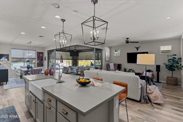 kitchen featuring an island with sink, hanging light fixtures, plenty of natural light, light hardwood / wood-style floors, and sink