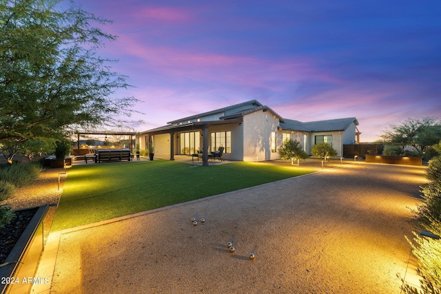 back house at dusk featuring a lawn and a hot tub