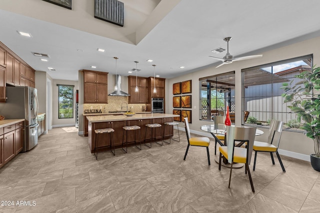 kitchen with stainless steel appliances, wall chimney range hood, a kitchen breakfast bar, pendant lighting, and a kitchen island