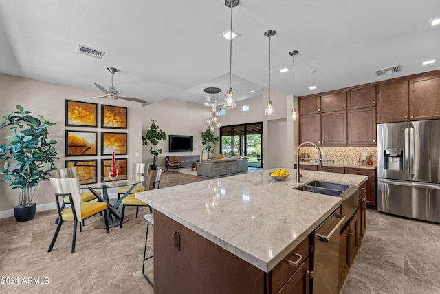 kitchen featuring ceiling fan, hanging light fixtures, stainless steel appliances, light stone counters, and a center island with sink