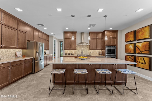 kitchen with decorative light fixtures, stainless steel appliances, a kitchen island with sink, and wall chimney exhaust hood