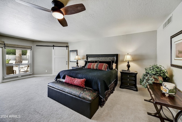 carpeted bedroom featuring ceiling fan, a barn door, and a textured ceiling