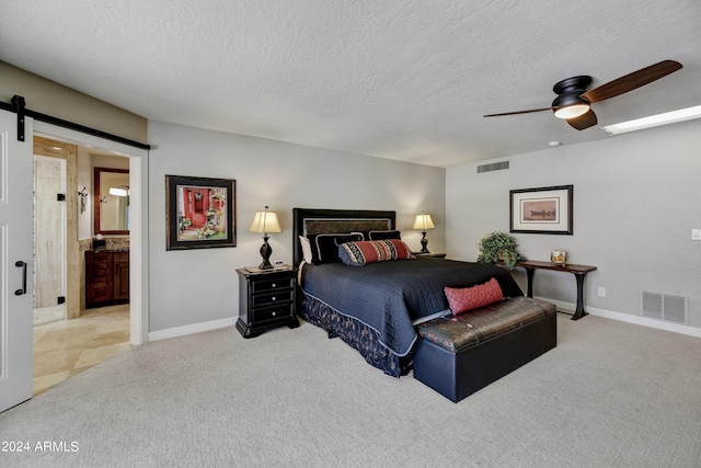 carpeted bedroom featuring a barn door, ceiling fan, a textured ceiling, and ensuite bathroom