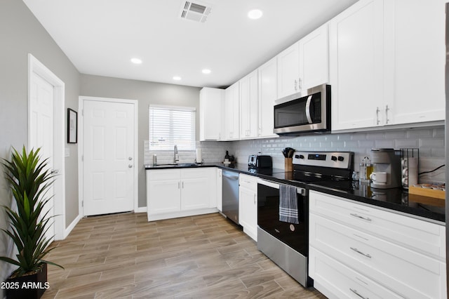 kitchen featuring stainless steel appliances, a sink, visible vents, tasteful backsplash, and dark countertops