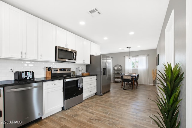 kitchen with tasteful backsplash, dark countertops, visible vents, appliances with stainless steel finishes, and white cabinetry