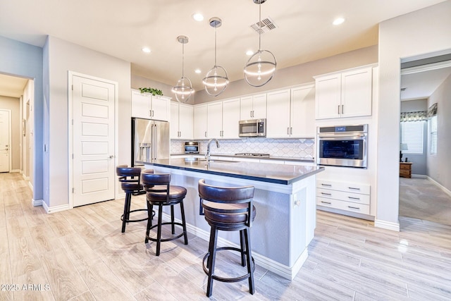 kitchen featuring appliances with stainless steel finishes, sink, pendant lighting, a center island with sink, and white cabinetry