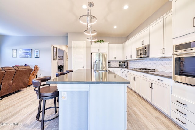 kitchen with white cabinets, a kitchen island with sink, stainless steel appliances, and hanging light fixtures