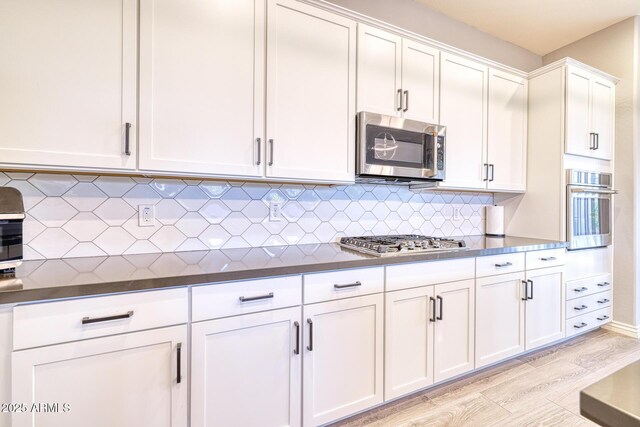 kitchen with white cabinets, decorative backsplash, stainless steel appliances, and light hardwood / wood-style floors