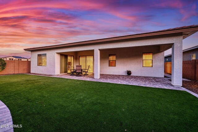 back house at dusk with a lawn and a patio