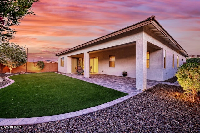 back house at dusk featuring a yard and a patio